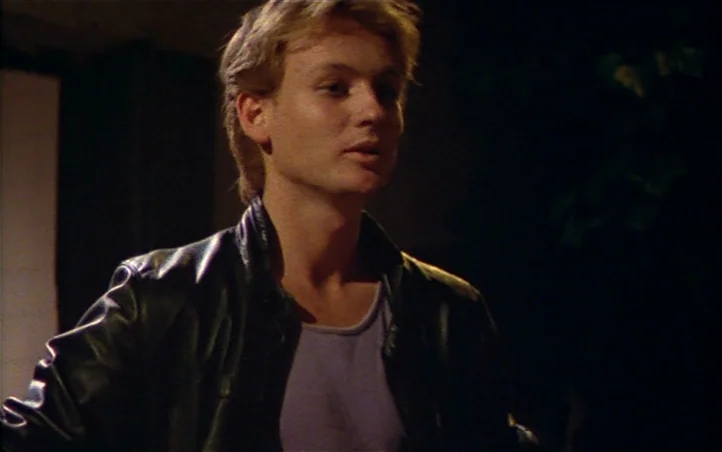 Pepi, Luci, Bom and Other Girls Like Mom (1980) movie still: medium — A man stands outdoors at night against a dark, nondescript background. He…