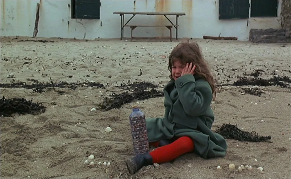 Kung Fu Master! (1988) movie still: fullbody — A stretch of sandy beach sits in front of a white wall with dark shutters. A young girl in a green…