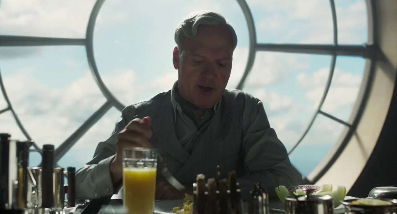 Dumbo (2019) movie still: medium — A man sits at a dining table before a large, circular, window-lined wall. He holds a fork while eating breakfast…