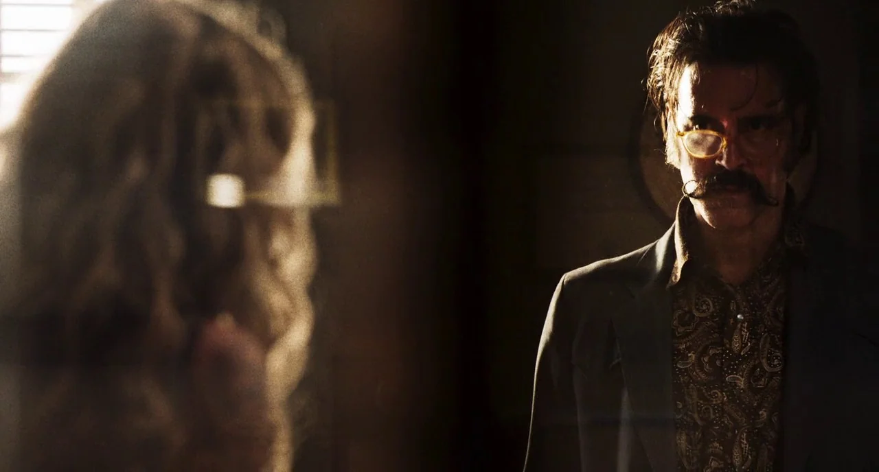 3 From Hell (2019) movie still: medium — A dark, dimly lit room with one individual in the foreground and one out-of-focus. The man in focus wears…