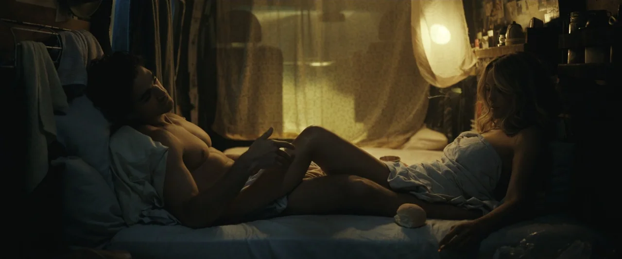 Dangerous Animals (2025) movie still: medium — A cramped, dimly lit van interior features a bed with white bedding and fabric curtains. A shirtless…