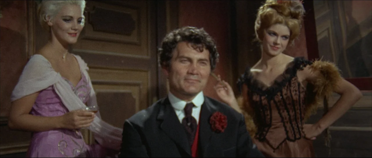 The Mercenary (1968) movie still: medium — An indoor room features dark wooden panels and red decorative accents on the walls. A man in a suit sits…