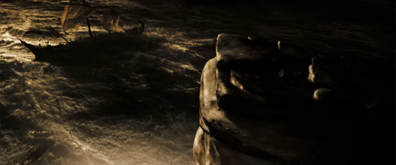 300 (2007) movie still: wide — A dark rocky outcrop overlooks a turbulent sea with a distant wooden warship. The ship travels through waves under a…