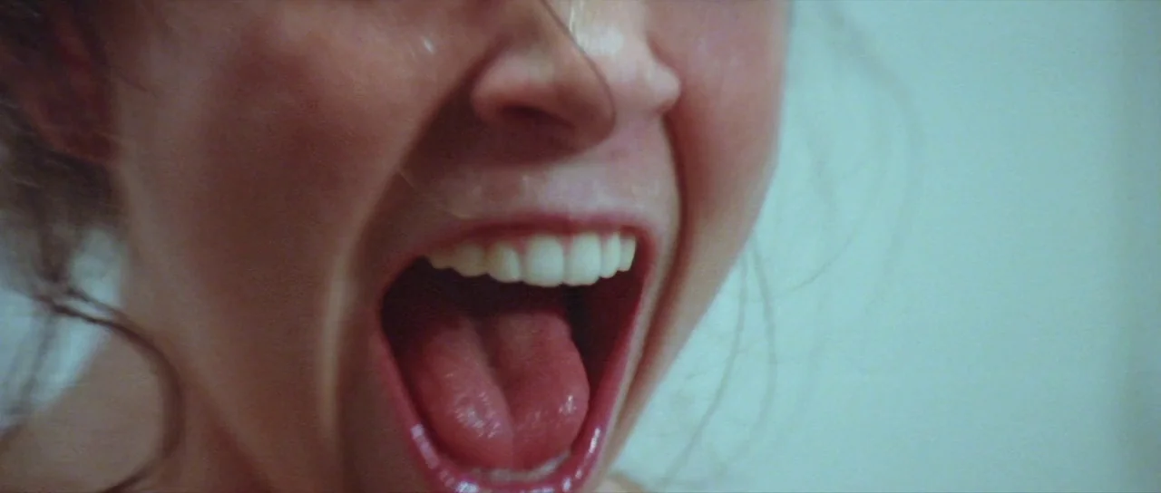 The Funhouse (1981) movie still: closeup — A close view shows the lower half of a face against a light wall. A person yells with their mouth fully…