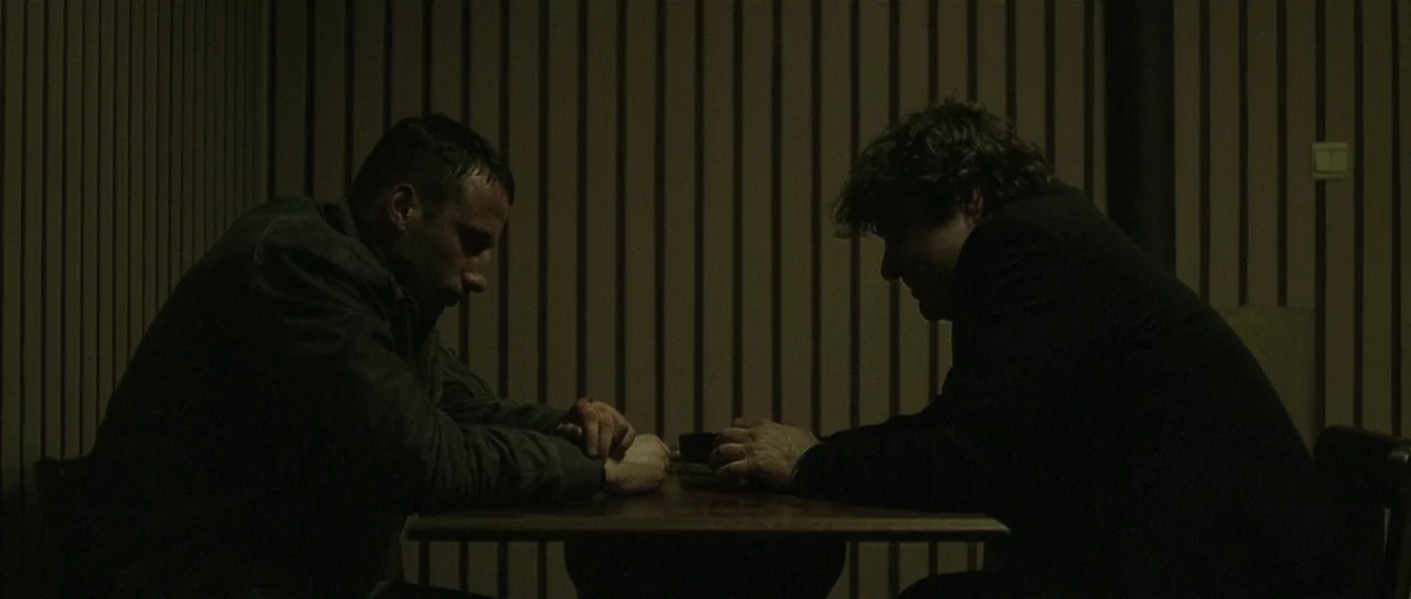 Bullhead (2011) movie still: medium — An interior space features wood-paneled walls and a small table between two seated men. The men face each…