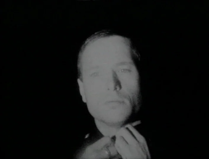 Cowards Bend The Knee (2003) movie still: closeup — A man stands in total darkness with his face sharply lit by a single source. He adjust his…