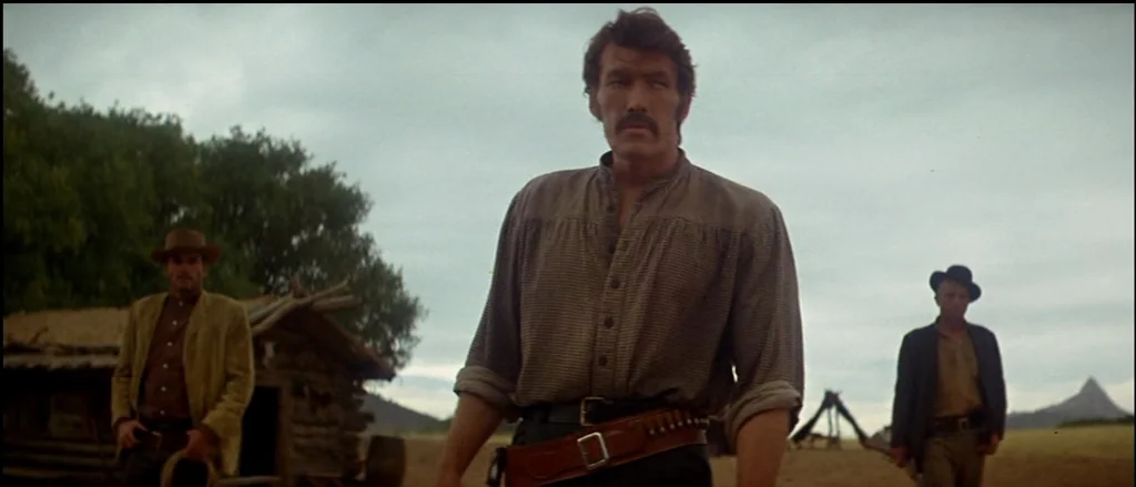Butch Cassidy and the Sundance Kid (1969) movie still: medium — A rural landscape features a wooden cabin under an overcast, grey sky. A man in the…