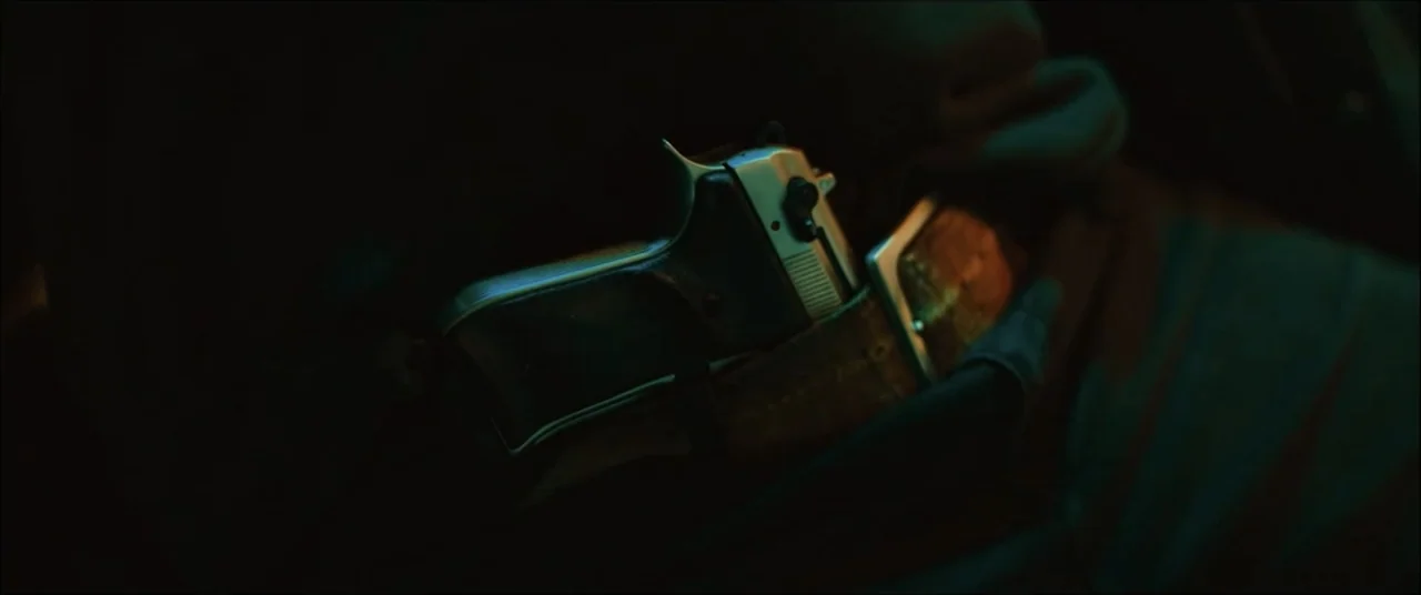 I'll Take Your Dead (2018) movie still: closeup — A close-up shot focuses on a silver and black handgun tucked into a leather belt. The weapon is…