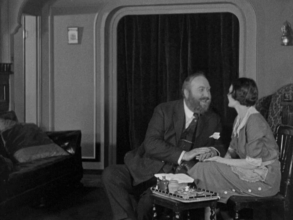 The Gold Rush (1925) movie still: medium — A 1920s parlor features an arched entryway with dark velvet curtains and dark furniture. A bearded man…