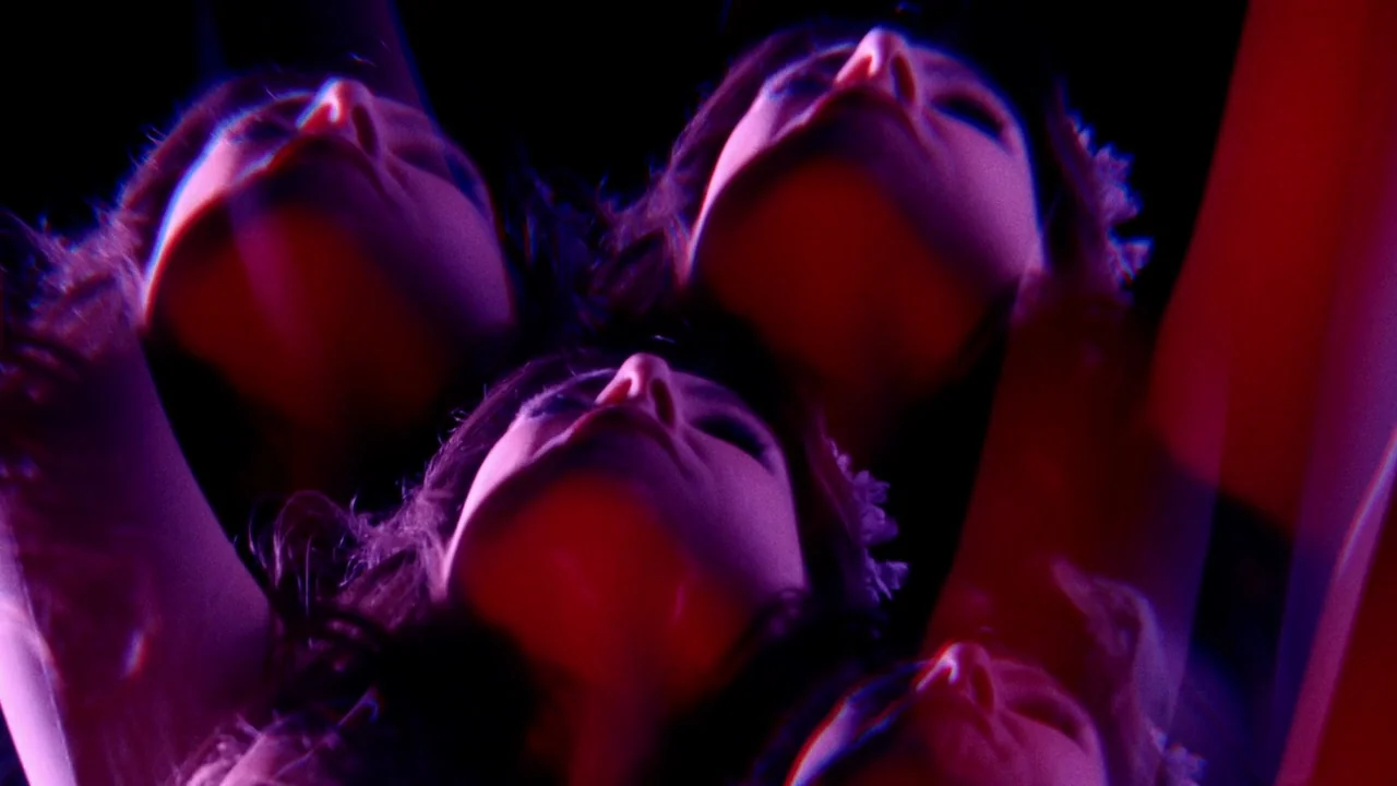 The Field Guide to Evil (2018) movie still: closeup — Three faces are tilted upward in a dark void filled with red and purple light. The composition…