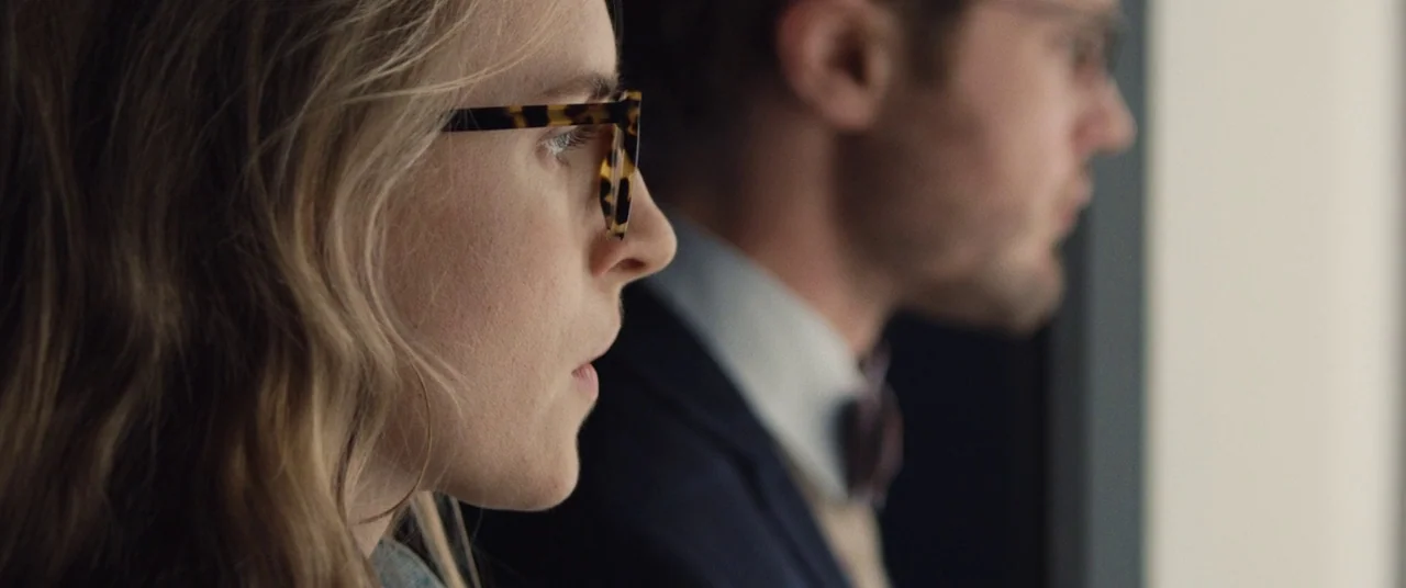 I Origins (2014) movie still: closeup — An office interior features two individuals positioned side-by-side looking towards a window. A woman with…