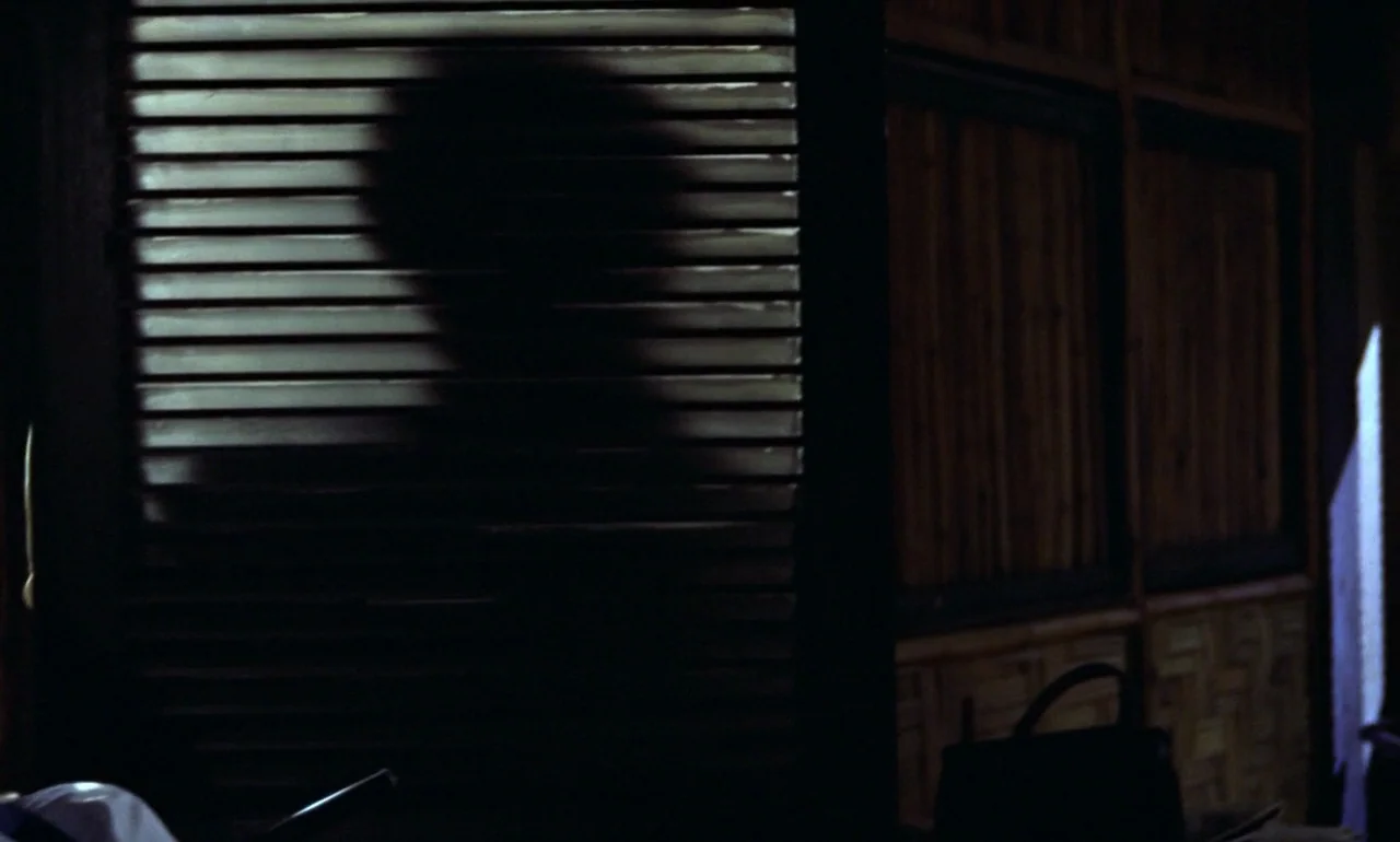 Dr. No (1962) movie still: medium — A dimly lit room features walls with textured panels and horizontal window blinds. A shadowy human silhouette is…
