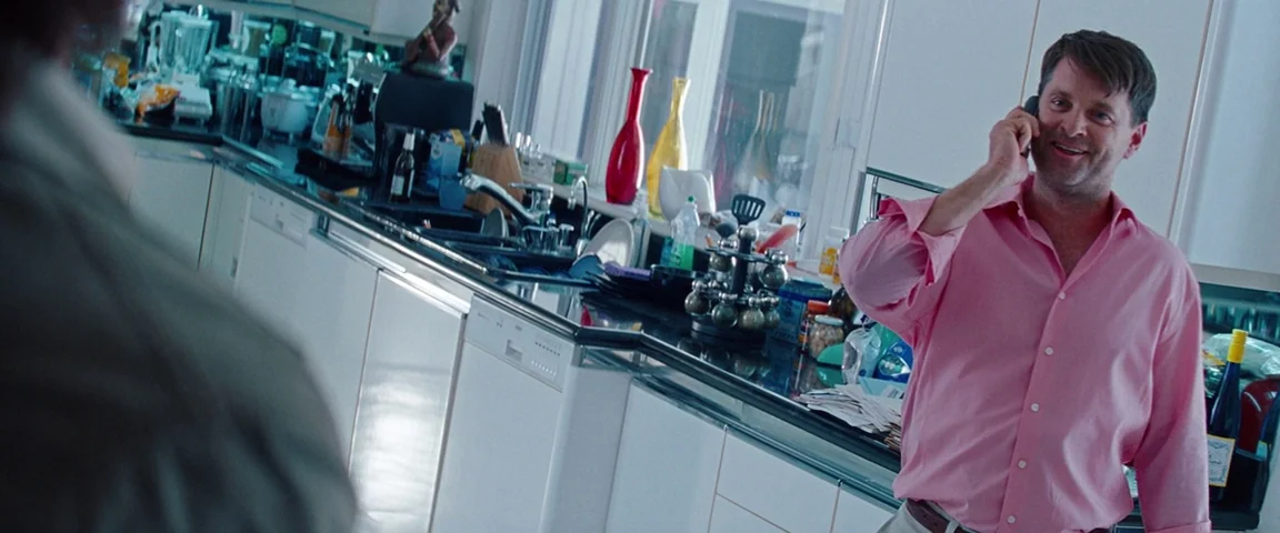 Savages (2012) movie still: medium — A well-lit residential space features white modern cabinetry and cluttered countertops. A man stands in the…