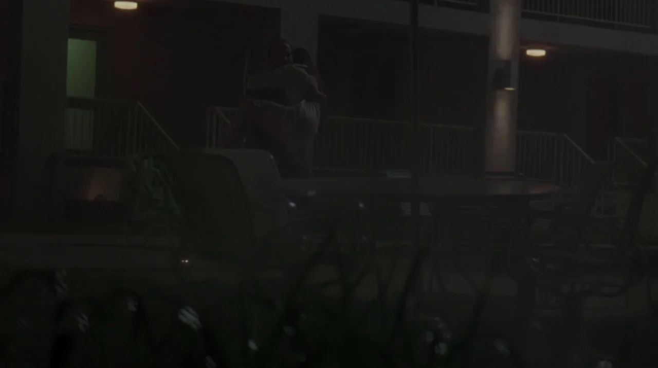 Lady in the Water (2006) movie still: wide — A dark outdoor motel courtyard at night features metal patio furniture and railings. A man carries a…