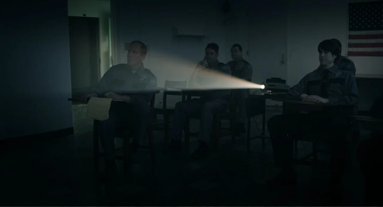 Ted Bundy: American Boogeyman (2021) movie still: medium — A dimly lit classroom features four men in uniforms sitting at wooden school desks. They…
