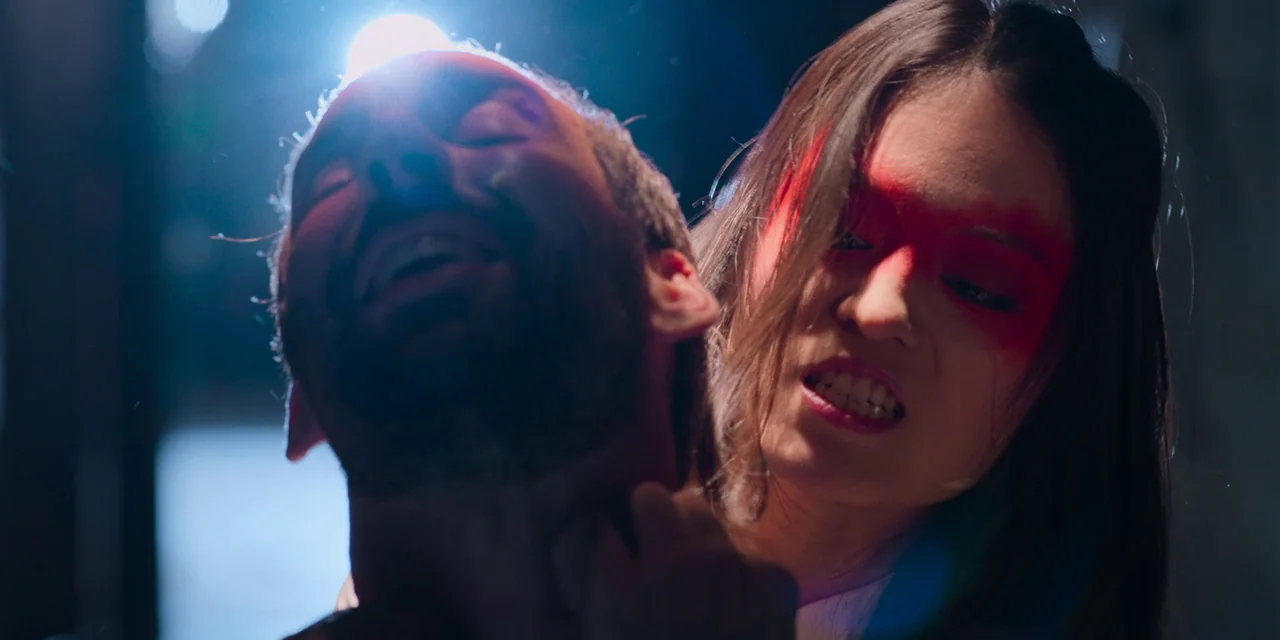 Sniper: G.R.I.T. (2023) movie still: closeup — A dark, dimly lit environment features a woman with prominent red eye makeup. She aggressively grips…