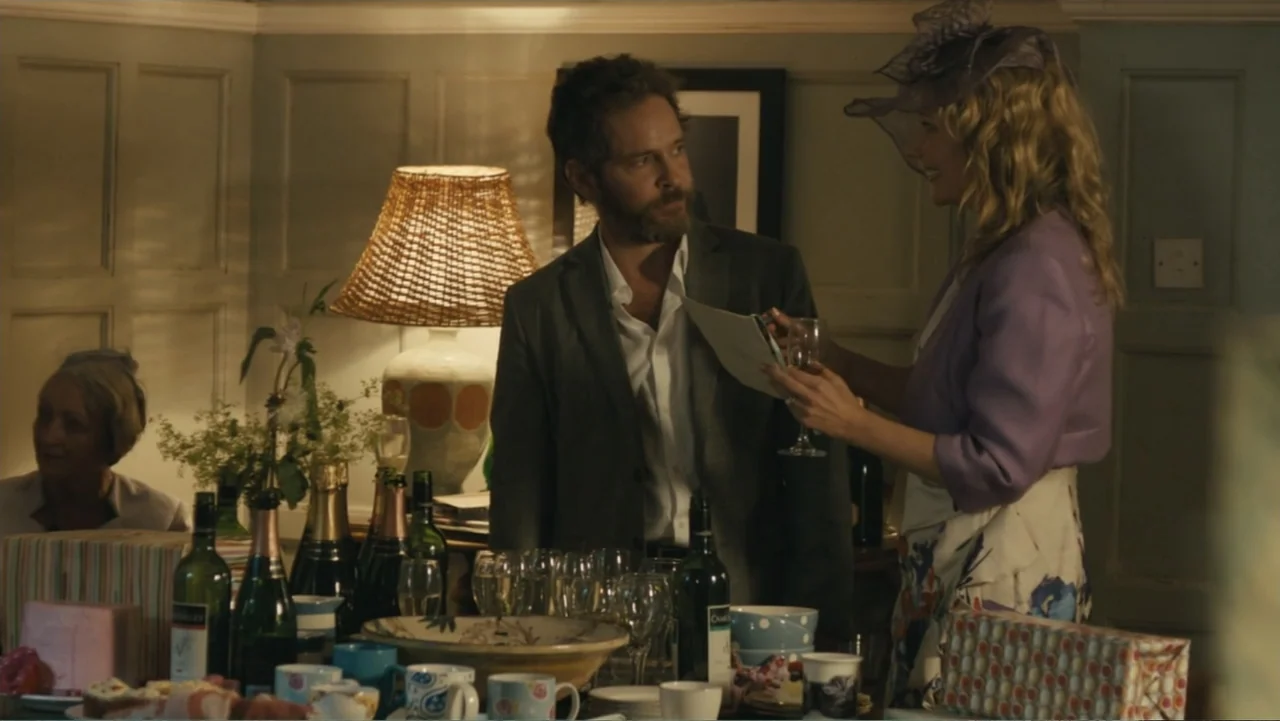 About Time (2013) movie still: medium — An interior living room is decorated for a gathering with numerous wine bottles and glassware. A man in a…