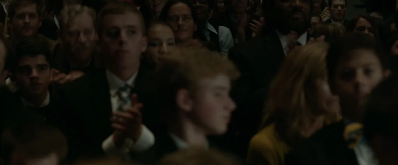 Coming Through the Rye (2016) movie still: medium — A dimly lit indoor auditorium contains a seated crowd of people in formal attire. Members of the…