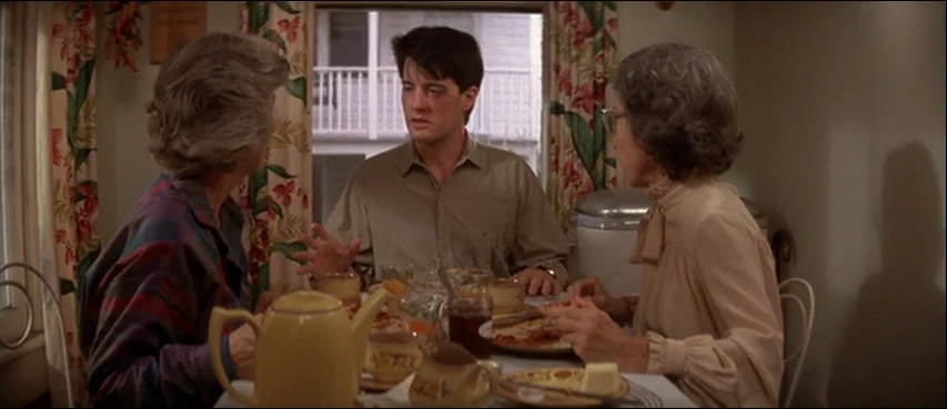 Blue Velvet (1986) movie still: medium — A breakfast nook features floral curtains and a table set with dishes. A young man sits between two older…