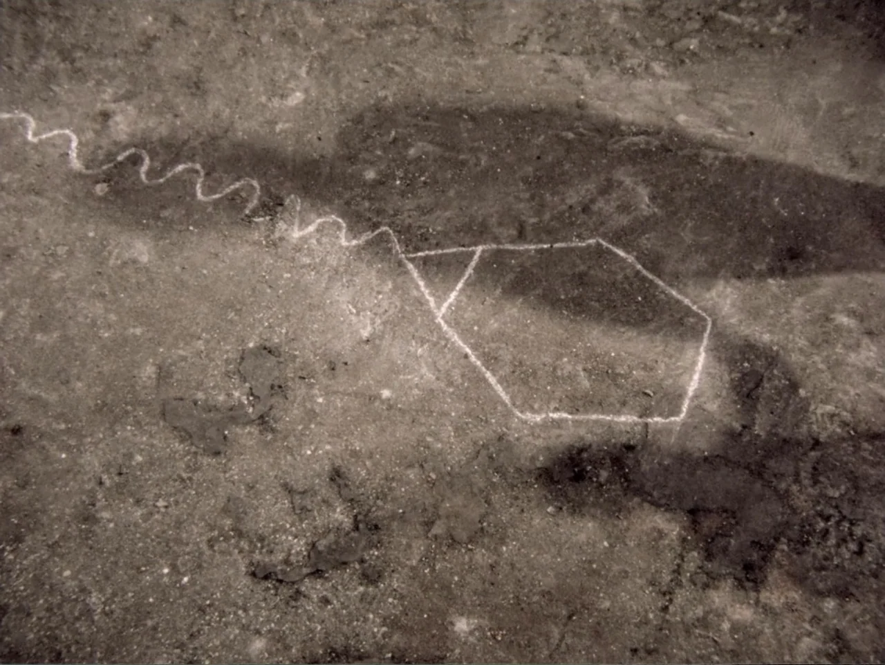 Don't Let Them Shoot the Kite (1989) movie still: closeup — A rough stone or dirt surface displays a white chalk geometric drawing. The white lines…