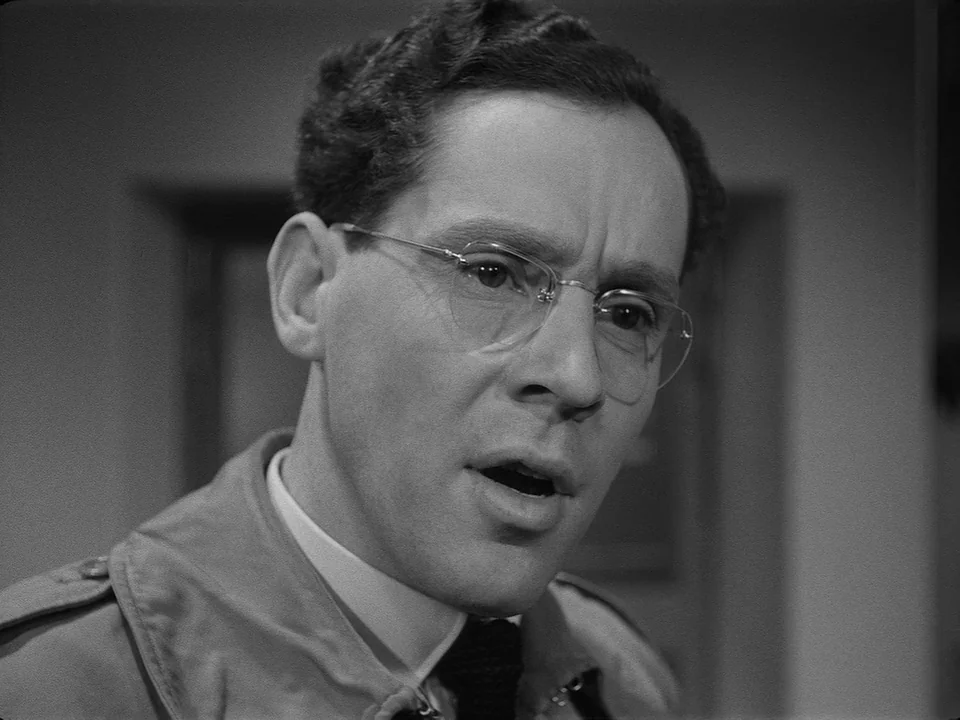 Brink of Life (1958) movie still: closeup — A man stands indoors against a muted, nondescript background. He turns his head three-quarters towards…