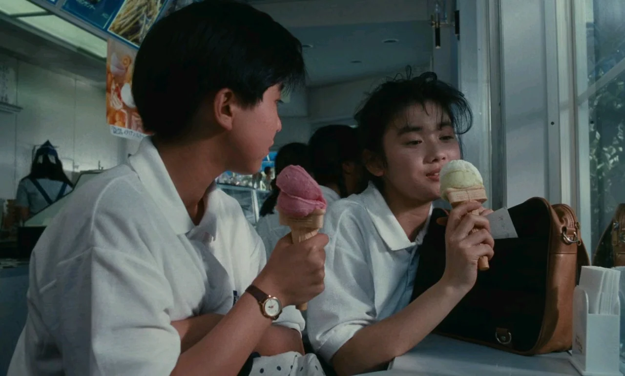 Chizuko’s Younger Sister (1991) movie still: medium — An ice cream shop features a counter where two young people sit together eating. The bright…