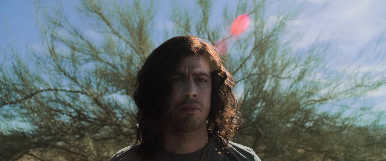 Destroyer (2018) movie still: closeup — A man stands outdoors in a desert environment with sparse vegetation in the background. The man looks…