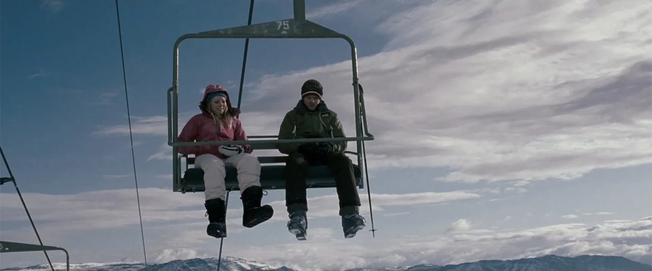Frozen (2010) movie still: fullbody — A metal chairlift carries two people across a bright, overcast snowy mountain landscape. A man and a woman in…