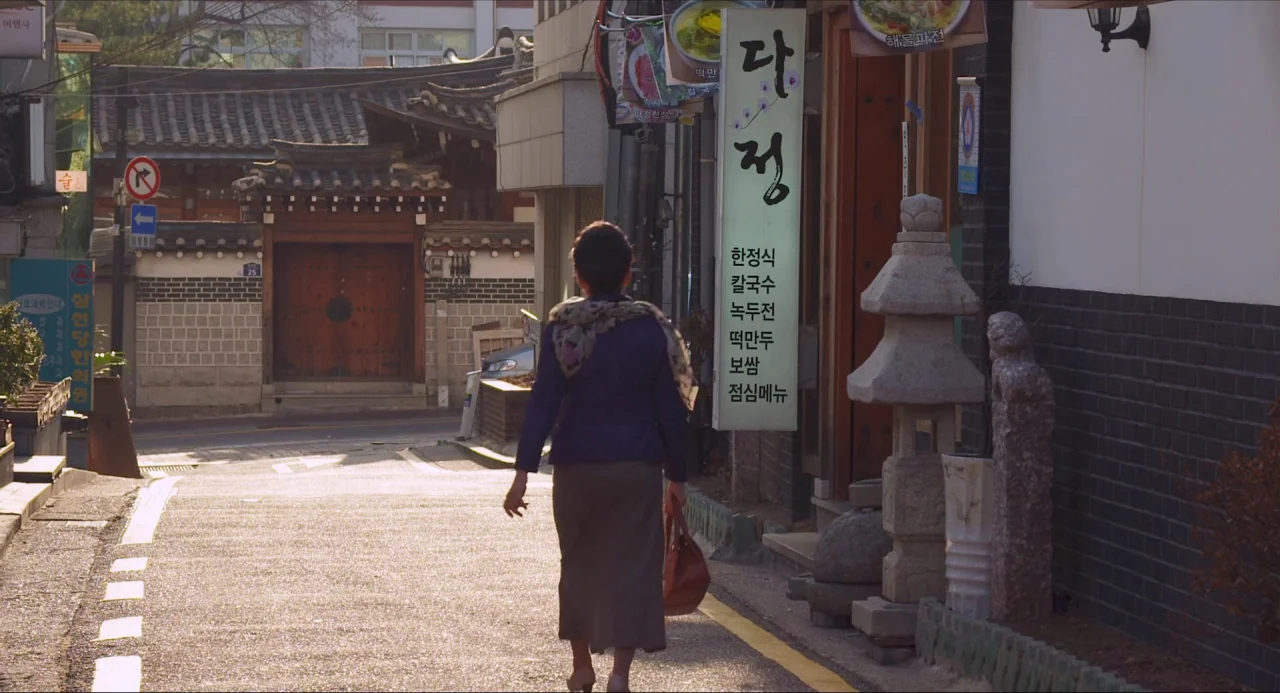 Nobody’s Daughter Haewon (2013) movie still: fullbody — A narrow paved street in Seoul features traditional Korean architectural elements and shop…