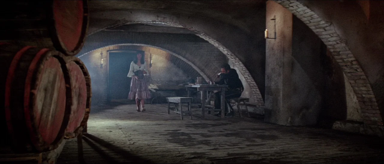Texas, Adios (1966) movie still: wide — A rustic brick wine cellar features vaulted ceilings and large wooden barrels in foreground. A woman in a…