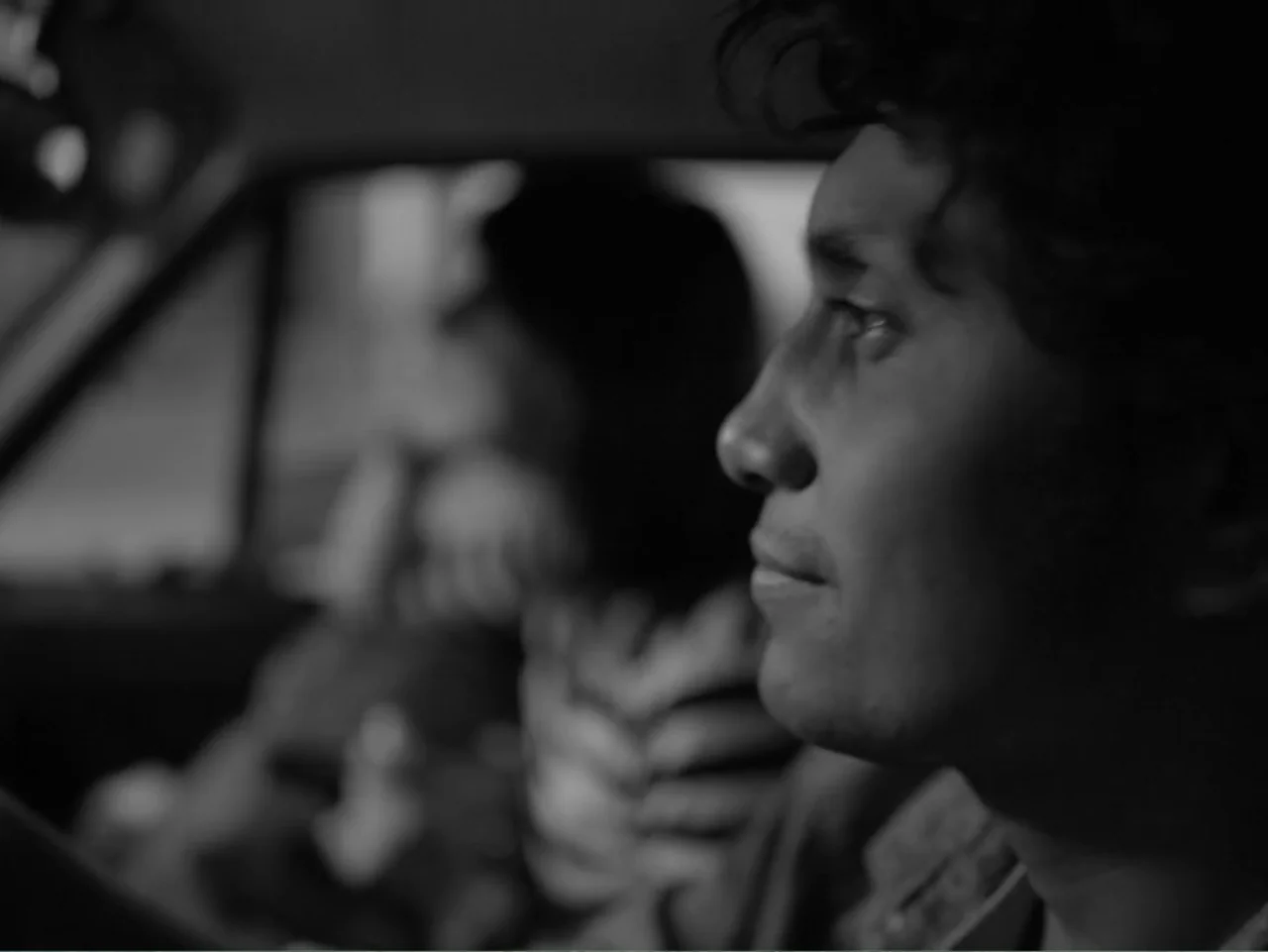 Güeros (2014) movie still: closeup — The interior of a vehicle at night with a blurred driver in the background. A young man sits in the passenger…