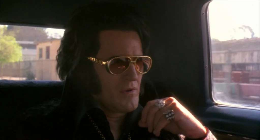 Bubba Ho-Tep (2002) movie still: closeup — A man resembling Elvis Presley sits in the passenger seat of a car. He is wearing gold-rimmed sunglasses…