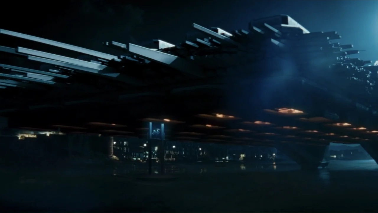 Robot Overlords (2015) movie still: wide — A massive, geometric metallic structure looms over a dark, wet sandy shoreline at night. Rows of warm…