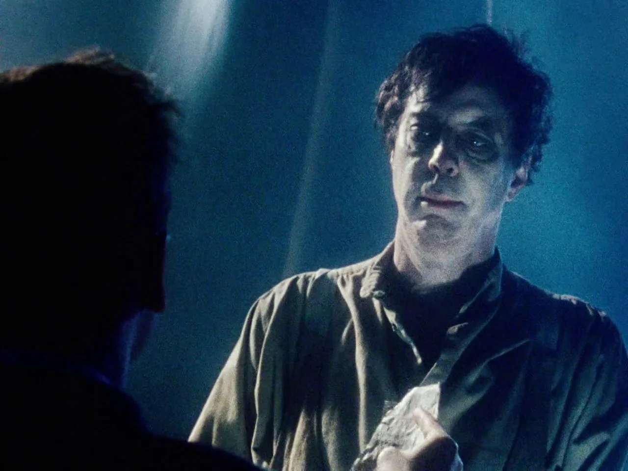 The Twentieth Century (2019) movie still: medium — A man stands in a dimly lit space with a blue-hued color palette. He looks toward an unseen…