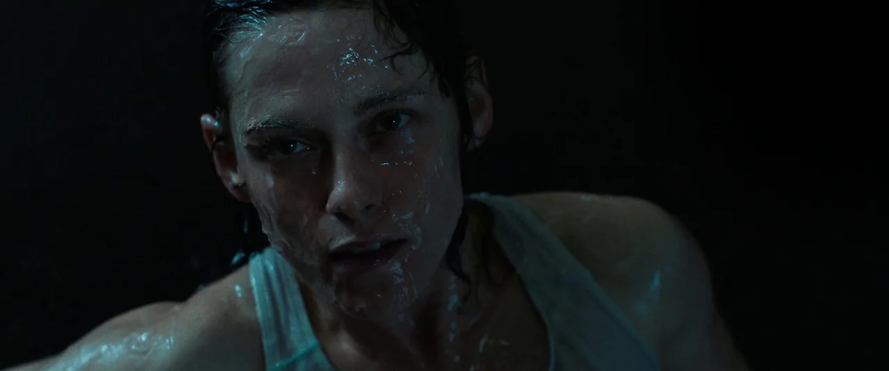 Love Lies Bleeding (2024) movie still: closeup — A dark, submerged environment surrounds a woman covered in water. Her head and shoulders occupy the…