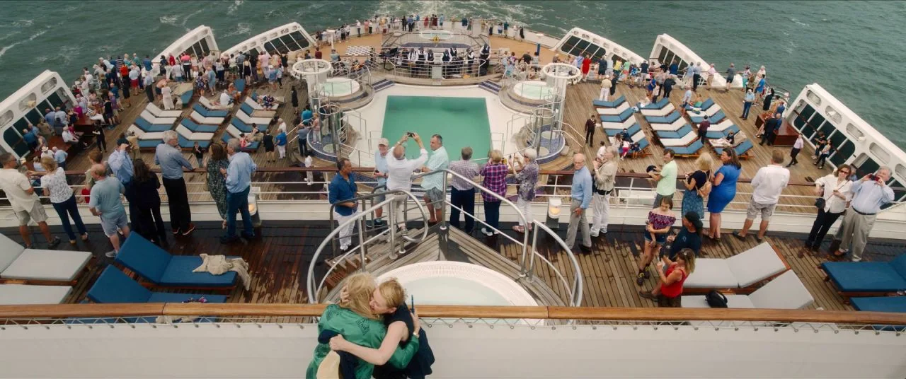 Let Them All Talk movie still: wide — The outdoor deck of a large cruise ship is filled with passengers near pools. Two women are standing at the…