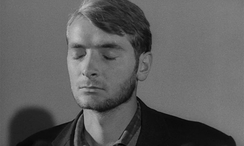 Man Is Not Bird (1965) movie still: closeup — A man stands before a featureless, flat-toned wall. He maintains a neutral expression with eyes closed.