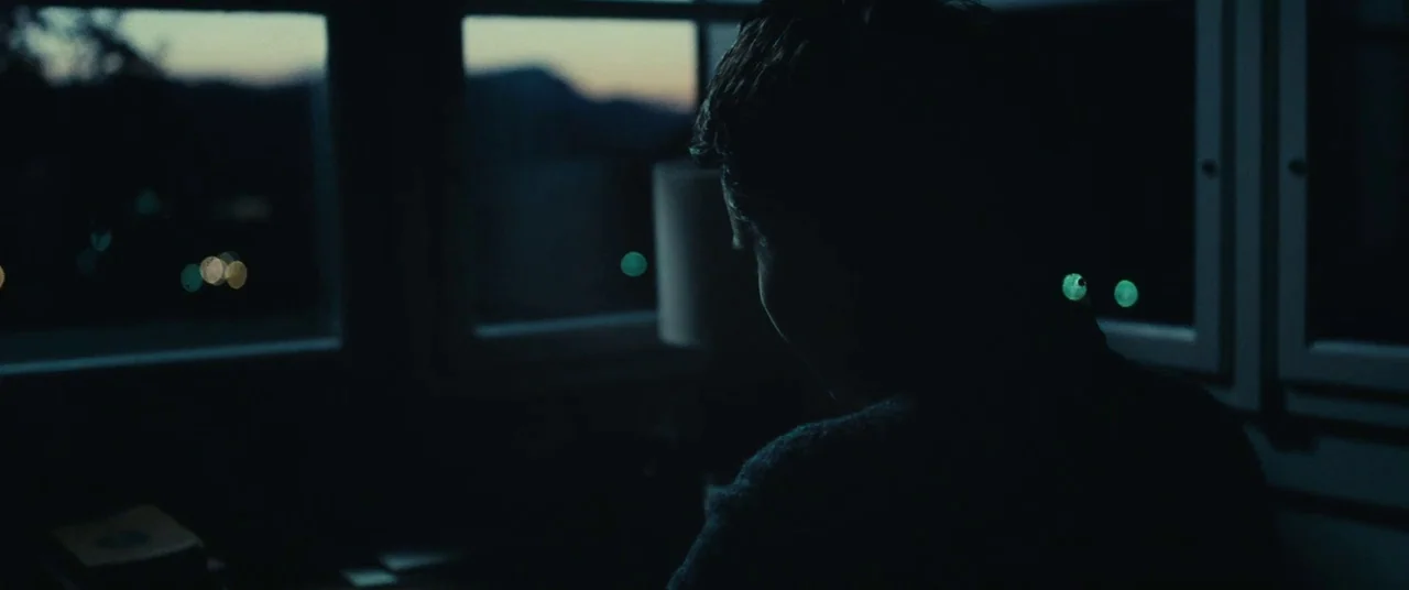 Clouds of Sils Maria (2014) movie still: medium — An interior space faces a large window overlooking a dark silhouette of mountains at dusk. A…