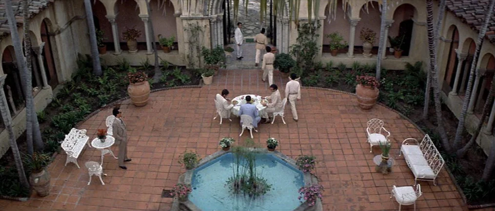 Scarface (1983) movie still: wide — An ornate courtyard features terracotta tiling, arched colonnades, and a central octagonal fountain. Several men…
