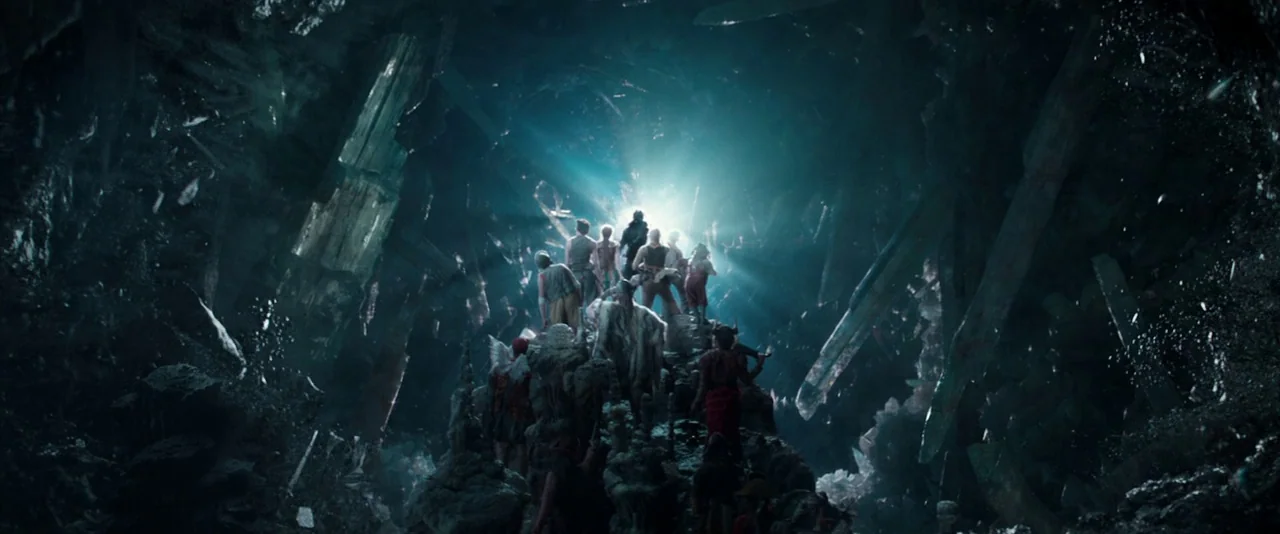 Pan (2015) movie still: wide — A dark, cavernous space is lined with massive, jagged translucent crystal formations. A group of people stands on a…
