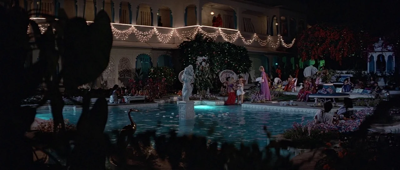 Octopussy (1983) movie still: wide — A luxury courtyard at night features a swimming pool decorated with fairy lights. People in evening attire…