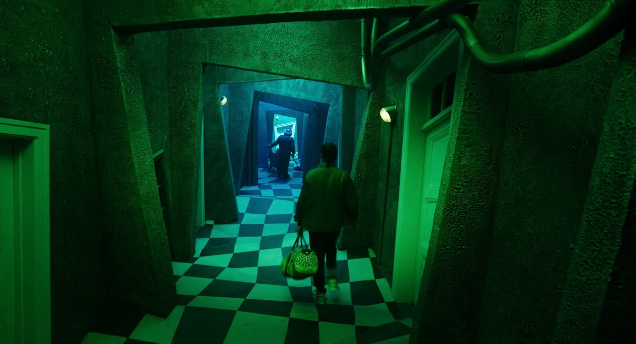 Beetlejuice Beetlejuice (2024) movie still: wide — A dark, distorted corridor features angled walls and a black-and-white checkered floor. A person…