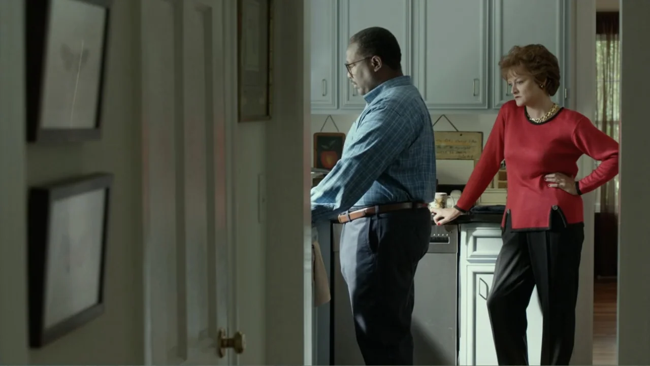 Confirmation (2016) movie still: medium — A residential room features light-colored cabinetry and a doorway in the foreground. A man stands at the…
