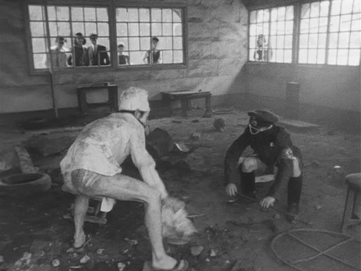 The War of Jan-Ken-Pon (1971) movie still: wide — A dilapidated, dusty structure with large multi-pane windows and a dirt-covered floor. Two men…