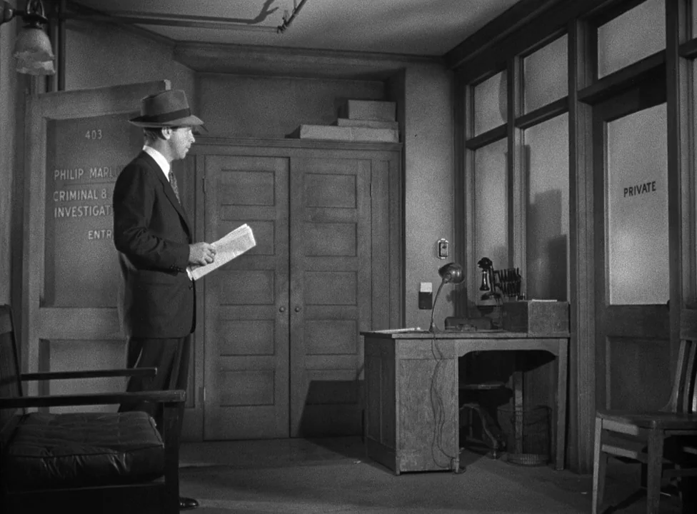 Murder, My Sweet (1944) movie still: medium — A mid-century private investigation agency features a wooden desk, two doors, and simple furniture. A…