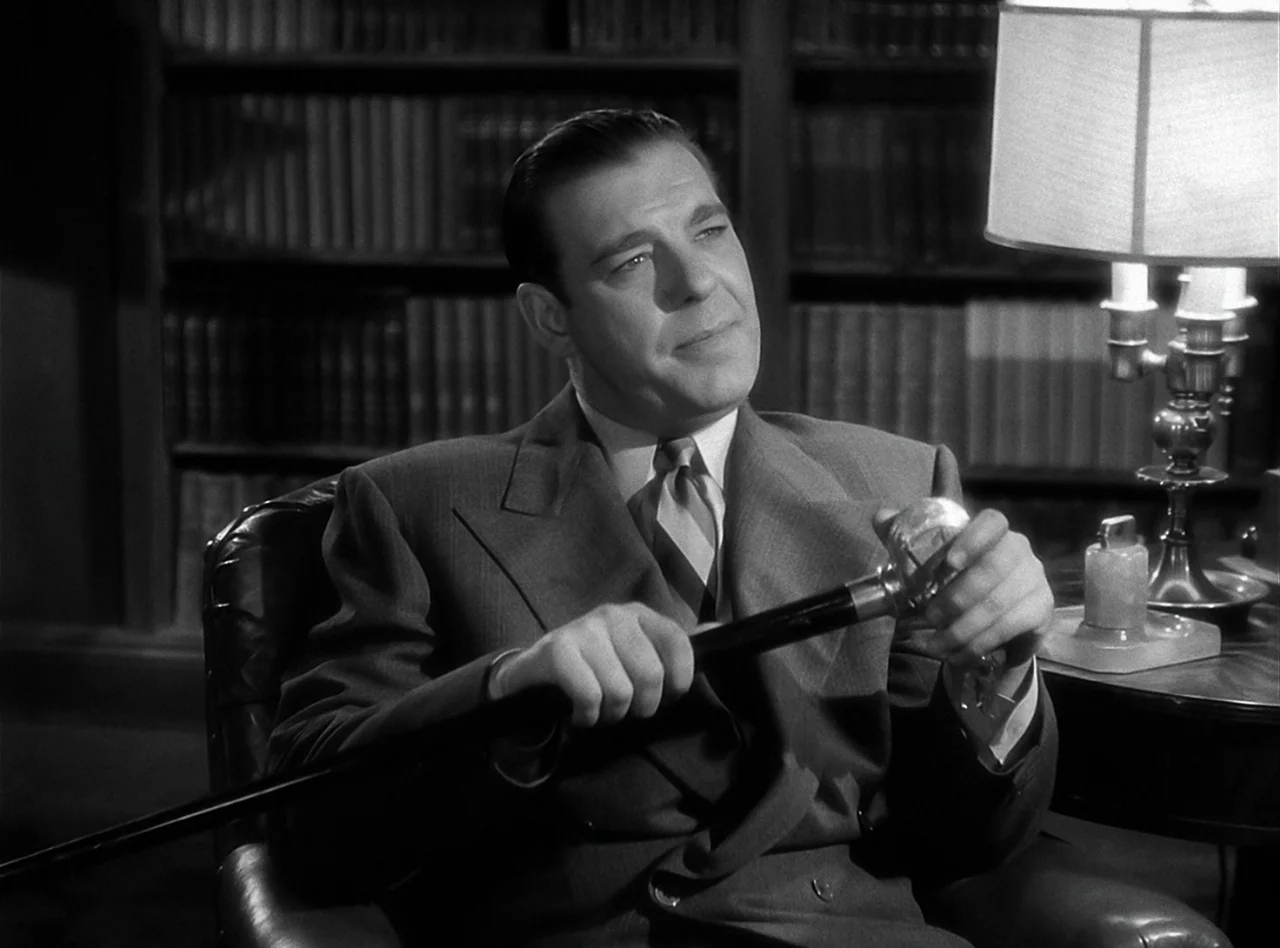 The Wolf Man (1941) movie still: medium — A man sits in a dark, wood-paneled room lined with numerous leather-bound books. He holds a black cane…