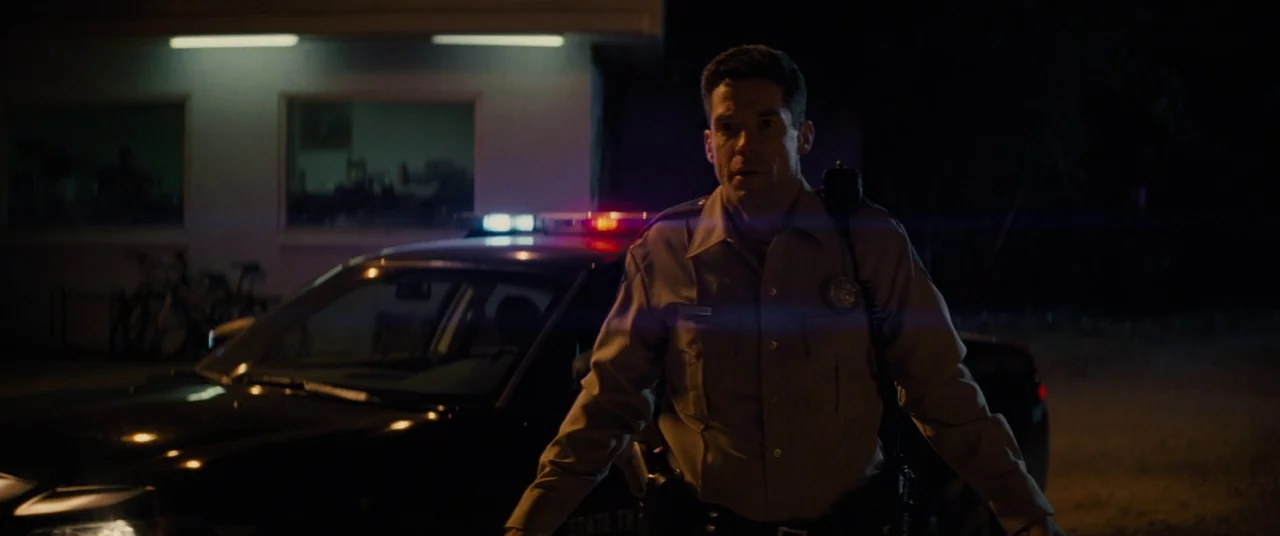 Midnight Special (2016) movie still: medium — A nighttime parking lot features a parked police car with active emergency lights. A uniformed state…