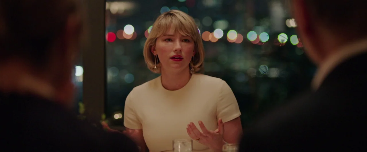 Swallow (2020) movie still: medium — A woman sits at a table in a dimly lit restaurant at night. She talks while gesturing with her hands against a…