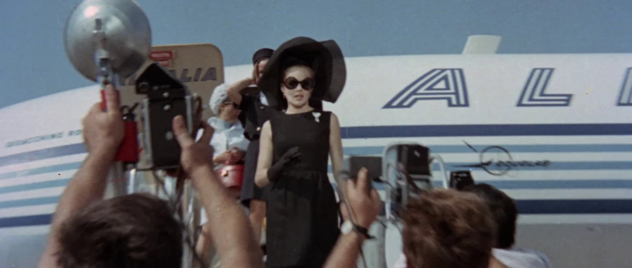 Orgasmo (1969) movie still: medium — An Alitalia airplane stands on the tarmac with a woman descending the mobile stairs. Photographers in the…