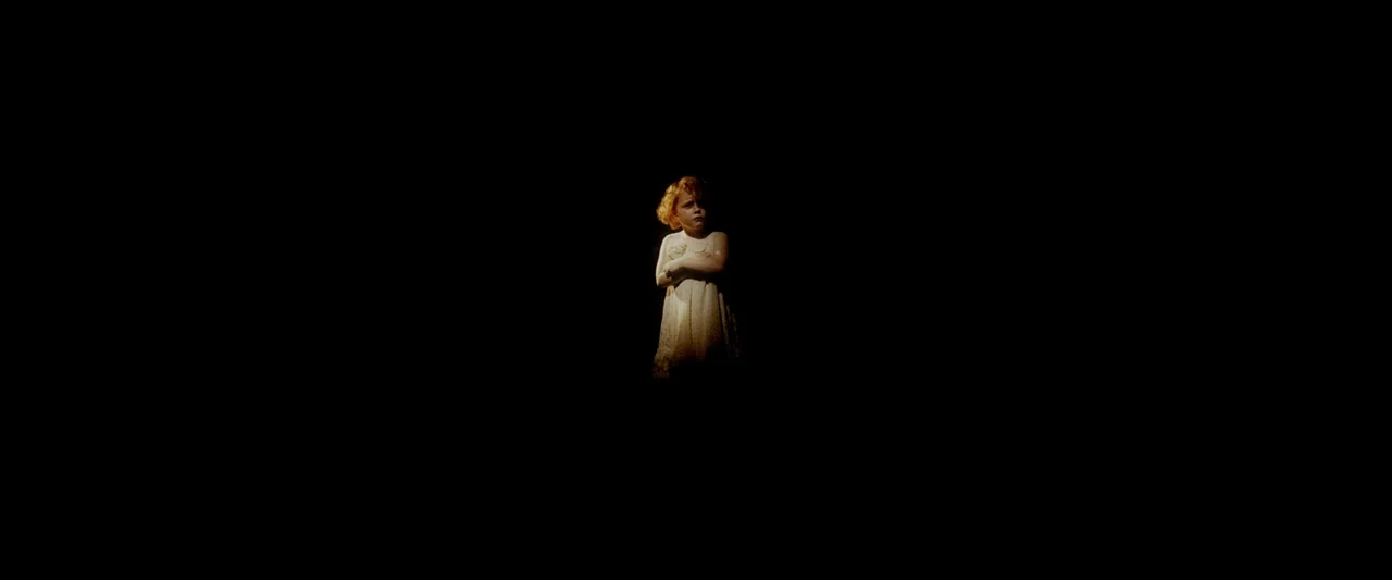 Moon Garden (2022) movie still: wide — A child stands in an undefined space completely enveloped by absolute black darkness. She stands isolated in…